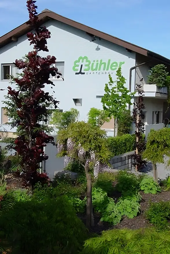 Skulptur zweier Hände in einem Garten, umgeben von üppigem Grün und bunten Blumen.